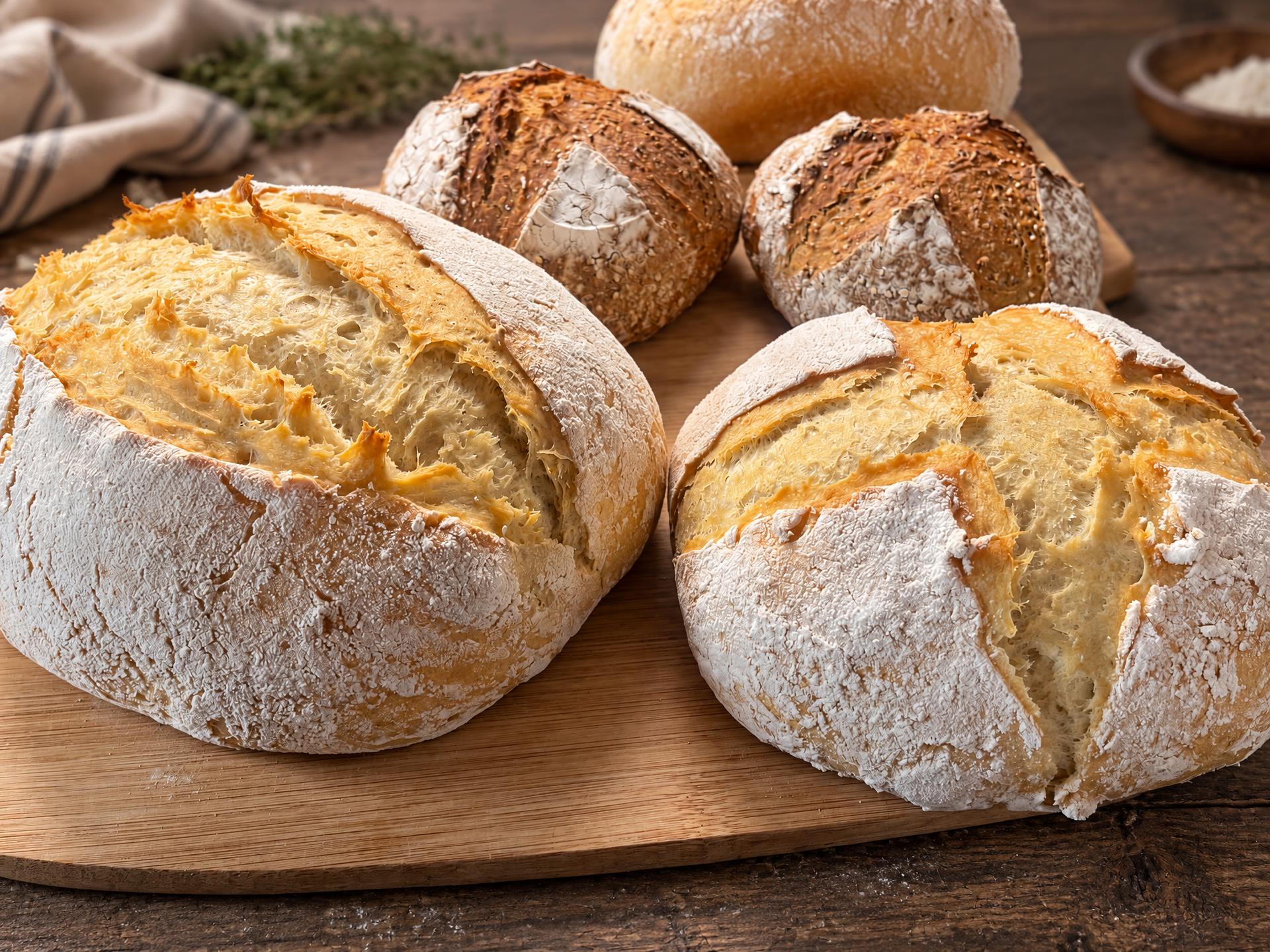 A board of sourdough boules in pale golden and seeded crusts