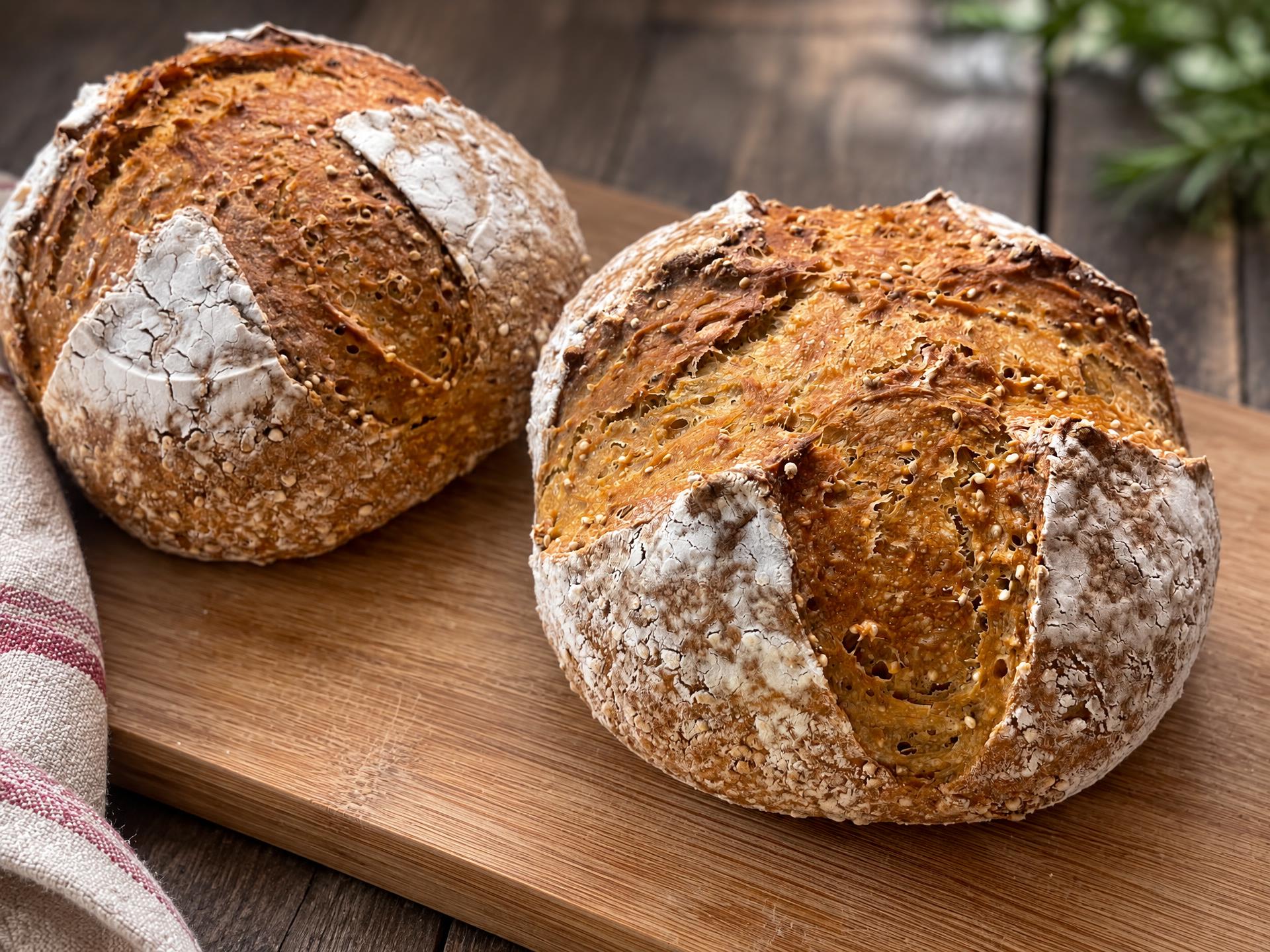 Two seed-crusted sourdough boules on a bamboo board